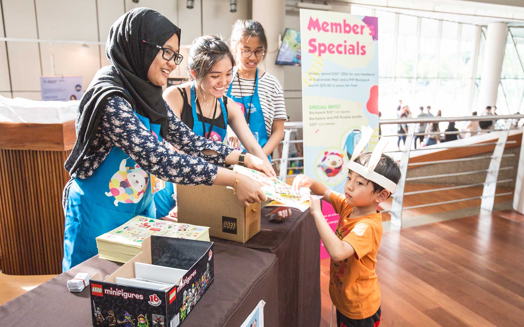 Image of volunteers manging a booth for Esplanade's PIP's Club membership and attending to a child.