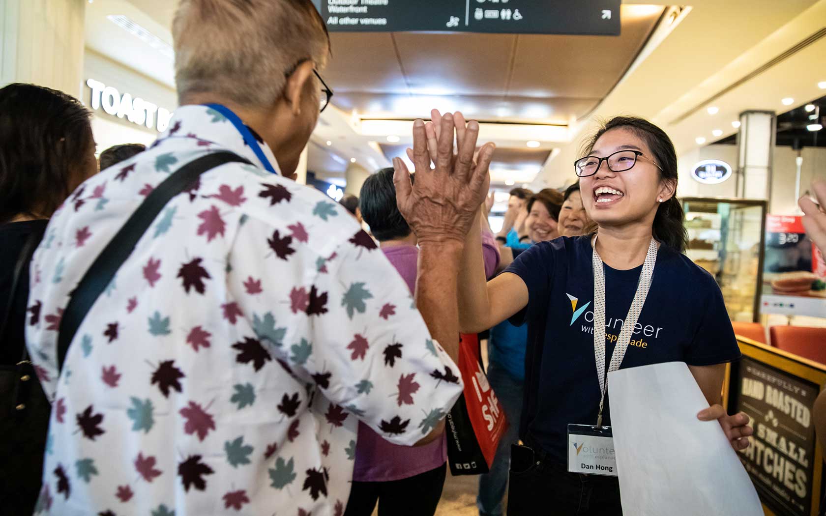 Image of a Welcome Ambassador giving a visitor a high-five around the entrance at Esplanade Mall.