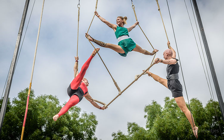 Three aerial acrobats hang from ropes in the air.