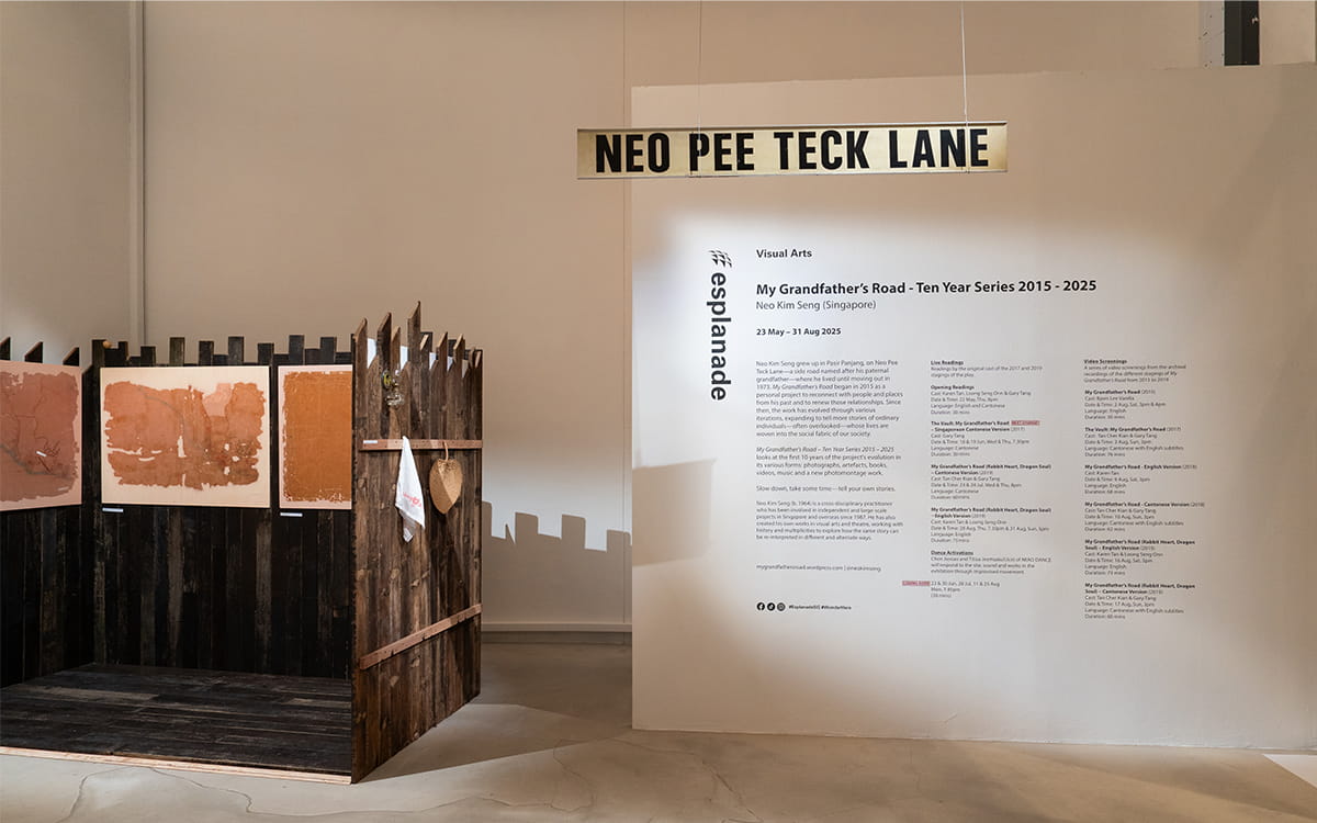 Installation view of My Grandfather’s Road – Ten Year Series 2015–2025 by Neo Kim Seng at Esplanade, featuring a wooden structure with earth-toned artworks and a large wall text detailing the exhibition. A sign reading “Neo Pee Teck Lane” hangs above, referencing the artist’s grandfather’s road.