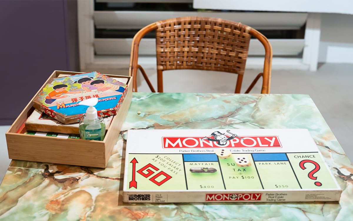 A tabletop display featuring a vintage Monopoly board game, a box of traditional children's games including one labeled "Marble Checkers," and a bottle of hand sanitizer.